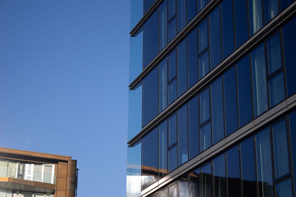 Reflective blue glass curtain wall of a modern building beside a bronze-clad block