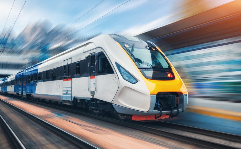 Modern white and yellow passenger train speeding past a station platform