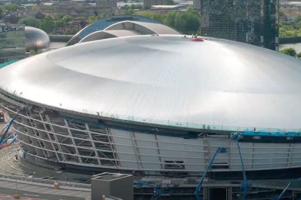 Aerial view of the OVO Hydro's silver domed roof with cherry pickers around the facade during construction
