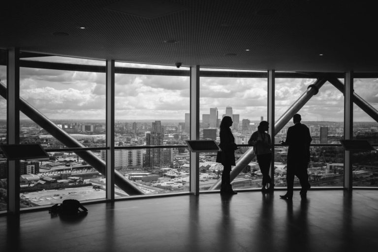 Black and white silhouettes of three people talking by floor-to-ceiling windows overlooking a city